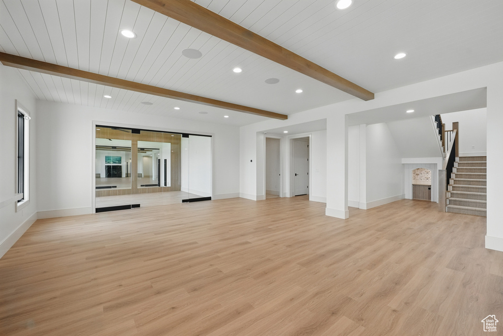 Unfurnished living room with recessed lighting, stairway, beam ceiling, light wood-type flooring, and baseboards