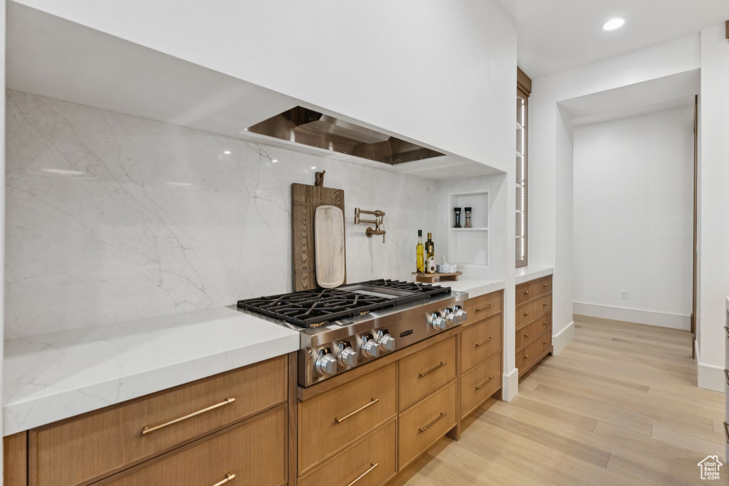 Kitchen with stainless steel gas stovetop, tasteful backsplash, light wood finished floors, ventilation hood, and light stone counters