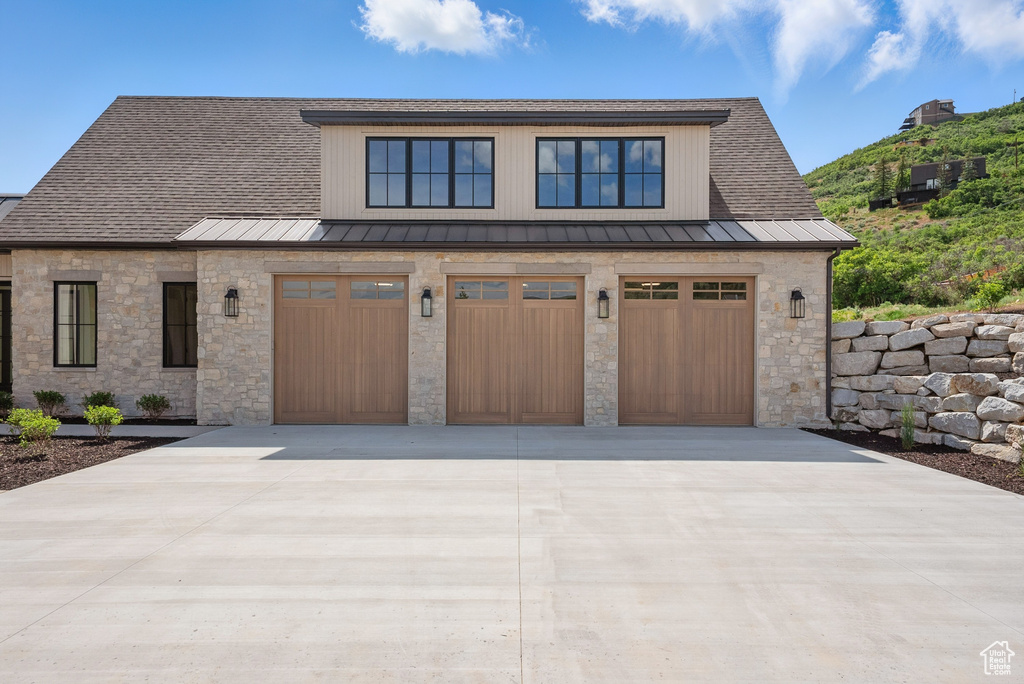 View of front facade featuring a standing seam roof, stone siding, driveway, and a garage