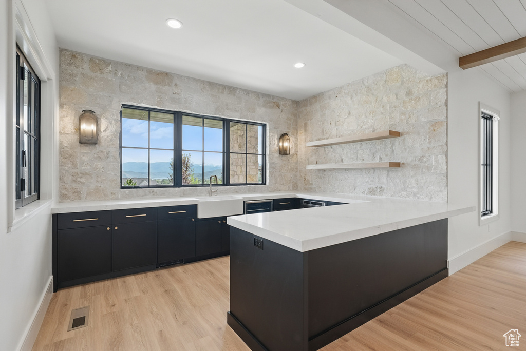 Kitchen with dark cabinetry, a sink, light countertops, decorative backsplash, and a peninsula