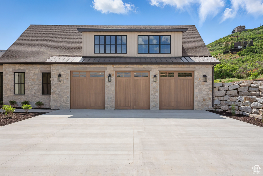 View of front facade featuring a standing seam roof, stone siding, driveway, and a garage
