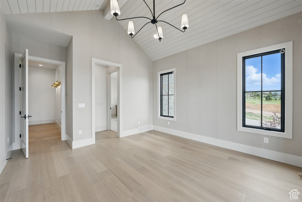 Empty room with light wood-type flooring, a chandelier, baseboards, high vaulted ceiling, and wood ceiling with exposed beams