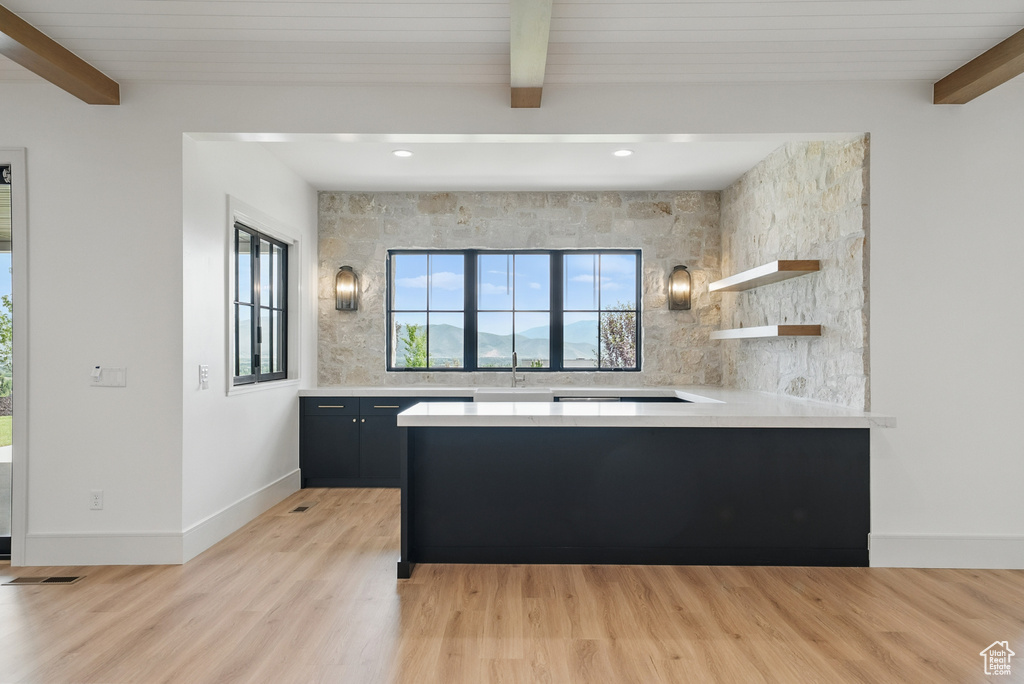 Kitchen with beam ceiling, light countertops, light wood-style flooring, a peninsula, and open shelves