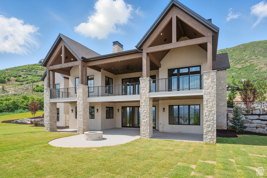 Back of property with a balcony, a patio area, a chimney, and a lawn