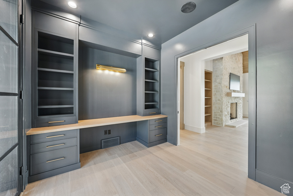 Unfurnished office with built in features, built in study area, light wood-style flooring, baseboards, and a stone fireplace