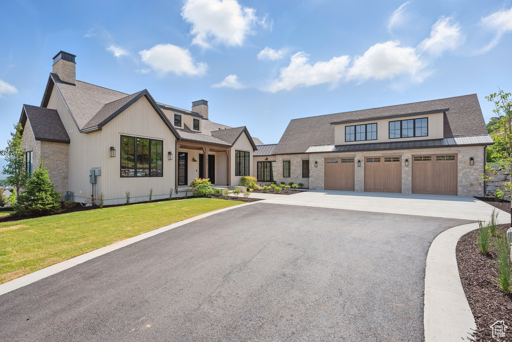 Modern farmhouse with a chimney, asphalt driveway, a standing seam roof, a front lawn, and a shingled roof