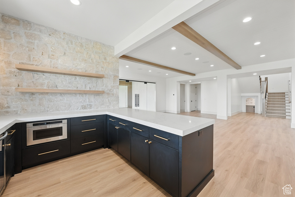 Kitchen featuring a peninsula, light wood-style floors, light countertops, beam ceiling, and tasteful backsplash