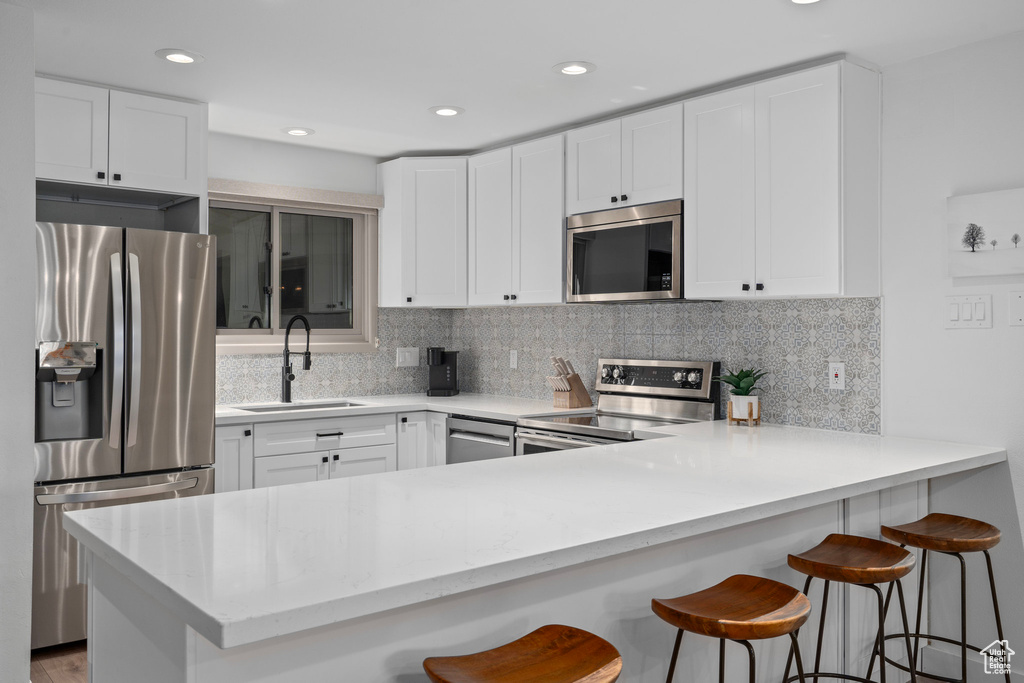 Kitchen featuring stainless steel appliances, white cabinetry, sink, kitchen peninsula, and a kitchen breakfast bar