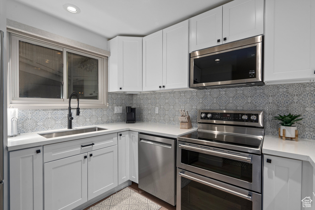 Kitchen featuring appliances with stainless steel finishes, tasteful backsplash, white cabinetry, and sink