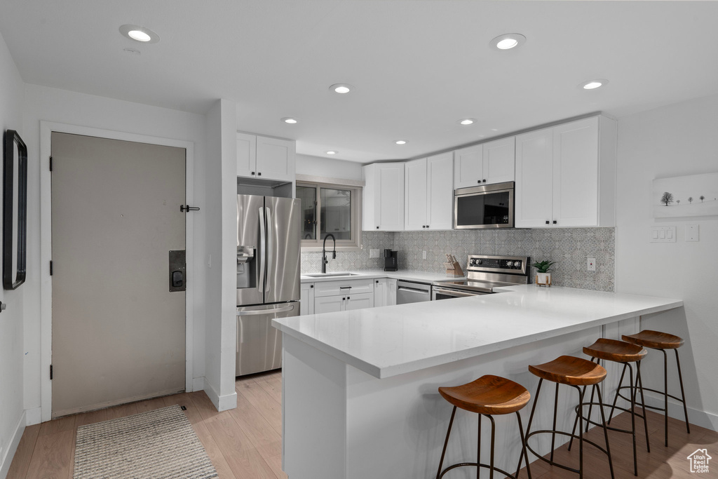 Kitchen featuring light wood-type flooring, white cabinetry, stainless steel appliances, a kitchen breakfast bar, and sink