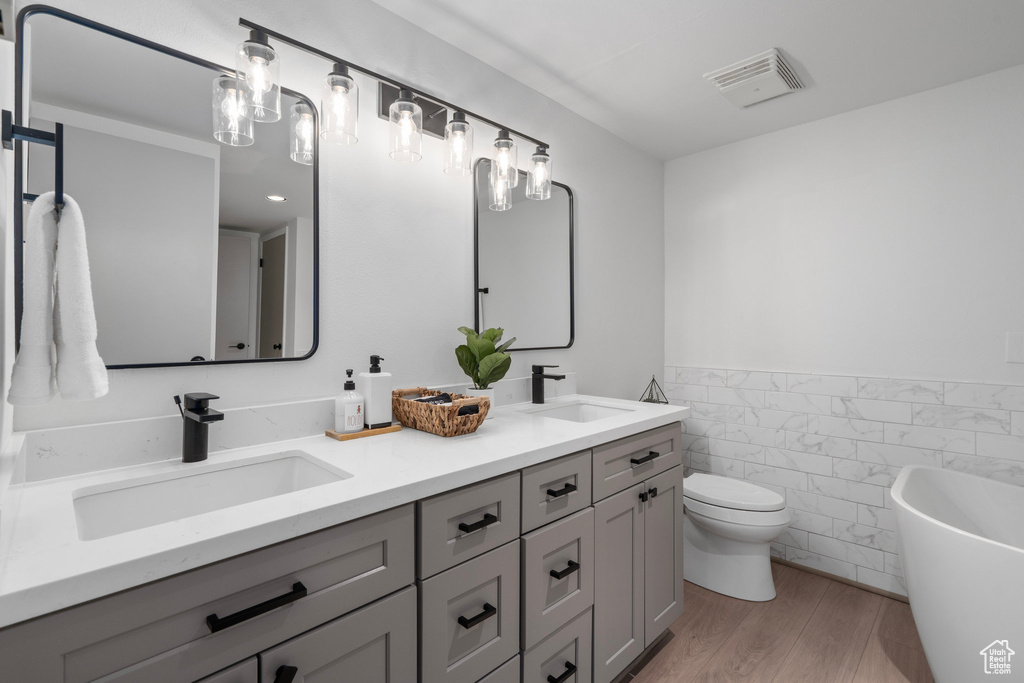 Bathroom with toilet, tile walls, wood-type flooring, a washtub, and vanity