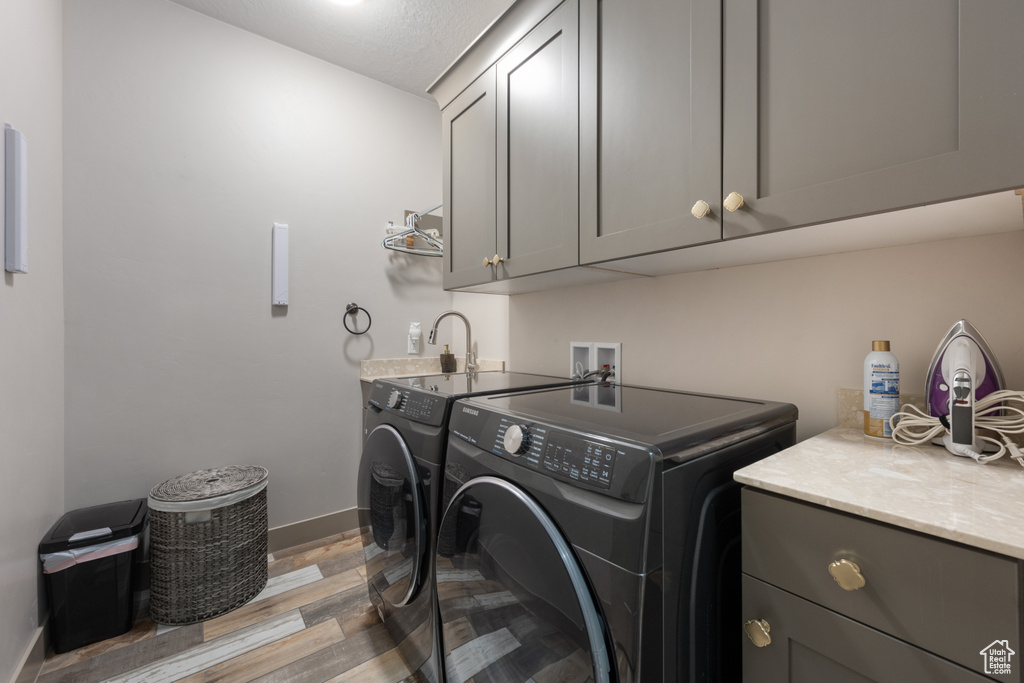 Laundry room with washing machine and clothes dryer, light hardwood / wood-style floors, cabinets, and sink