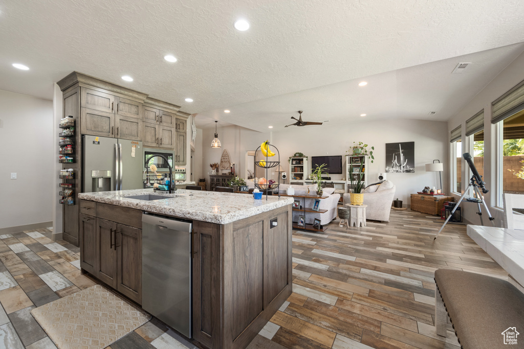 Kitchen featuring vaulted ceiling, hardwood / wood-style floors, an island with sink, stainless steel appliances, and sink