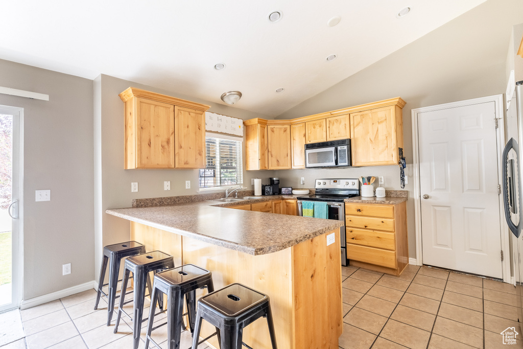 Kitchen with appliances with stainless steel finishes, vaulted ceiling, a breakfast bar area, and kitchen peninsula