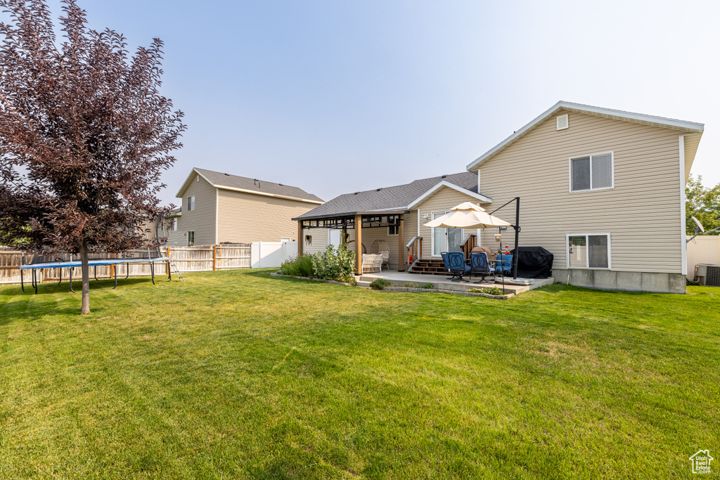 Rear view of property with a trampoline, central AC unit, a lawn, and a patio area