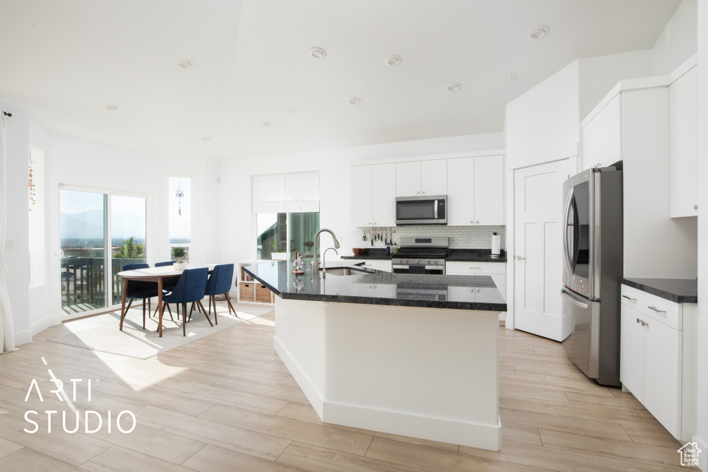 Kitchen with light wood-type flooring, appliances with stainless steel finishes, a center island with sink, and sink