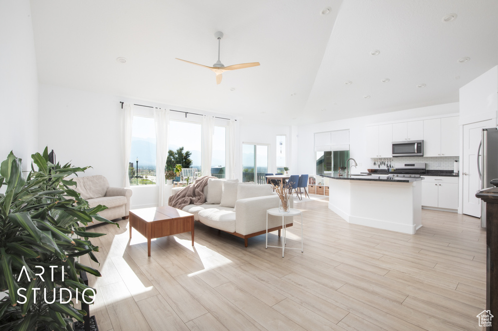 Living room featuring high vaulted ceiling, ceiling fan, sink, and light wood-type flooring