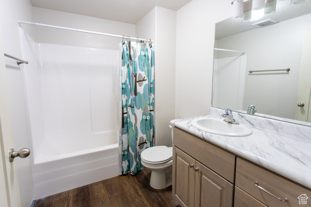 Full bathroom with toilet, wood-type flooring, shower / tub combo with curtain, vanity, and a textured ceiling