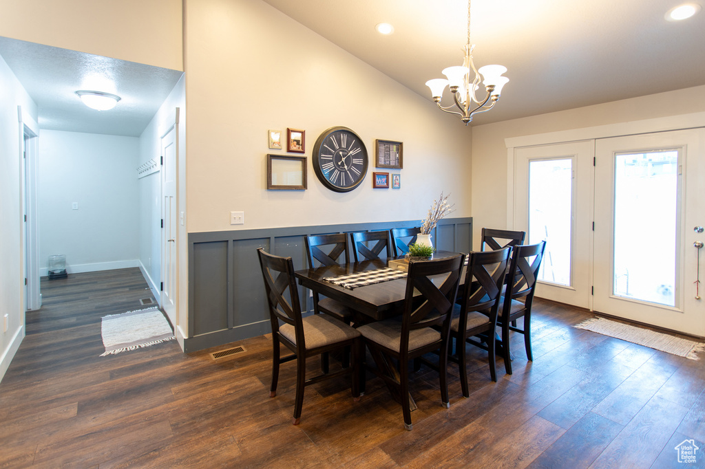 Dining room featuring dark wood-type flooring, vaulted ceiling, and an inviting chandelier