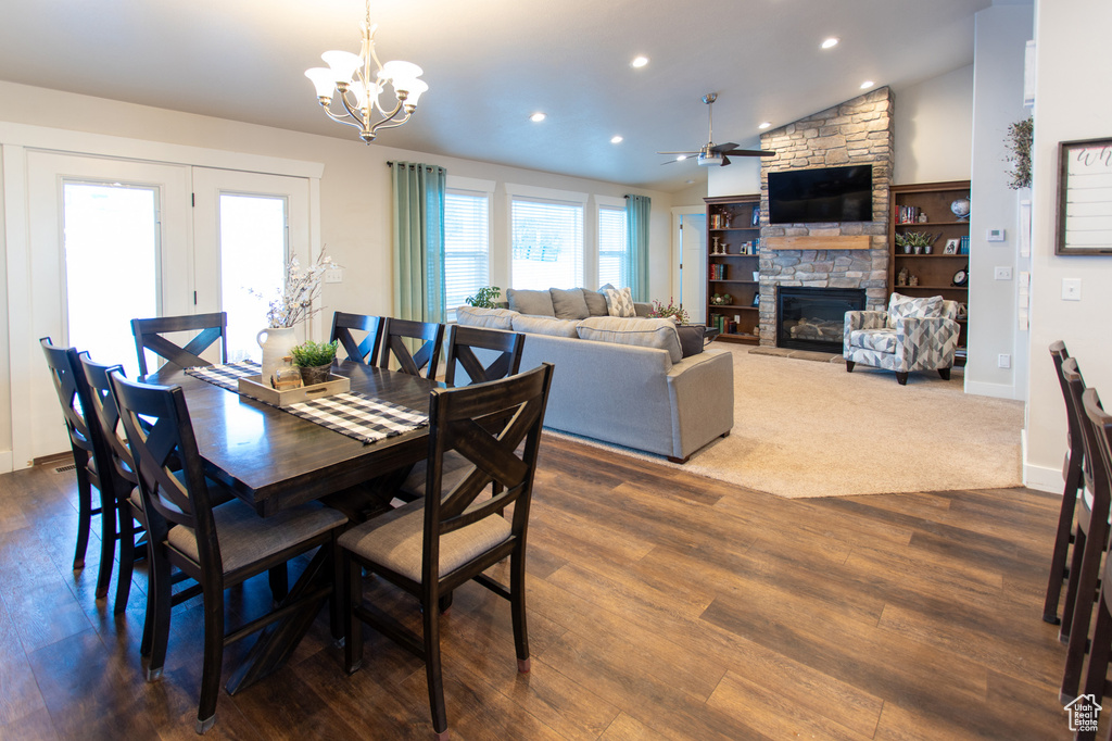 Dining area with ceiling fan with notable chandelier, a fireplace, dark hardwood / wood-style floors, and vaulted ceiling