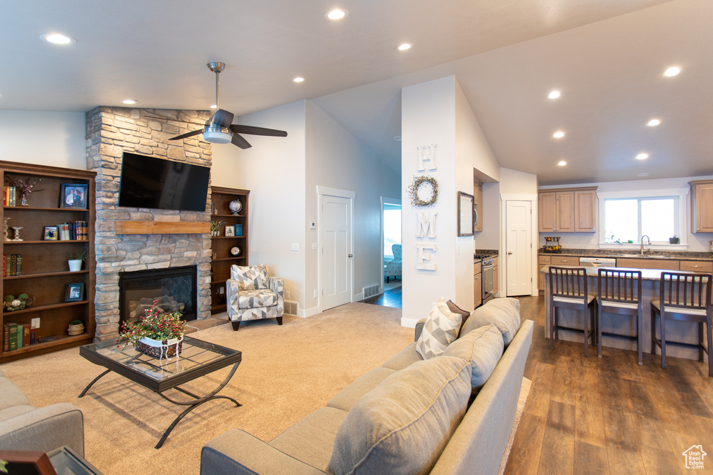 Living room featuring hardwood / wood-style floors, a stone fireplace, sink, high vaulted ceiling, and ceiling fan