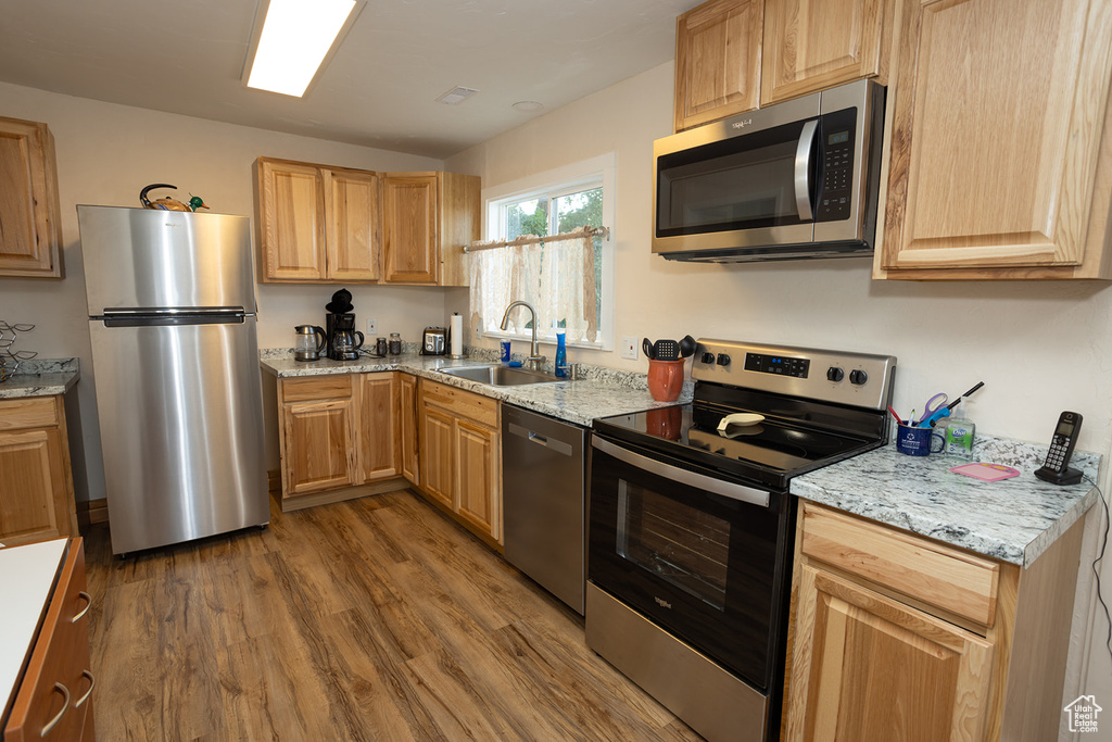 Kitchen with light hardwood / wood-style flooring, sink, light stone countertops, and appliances with stainless steel finishes