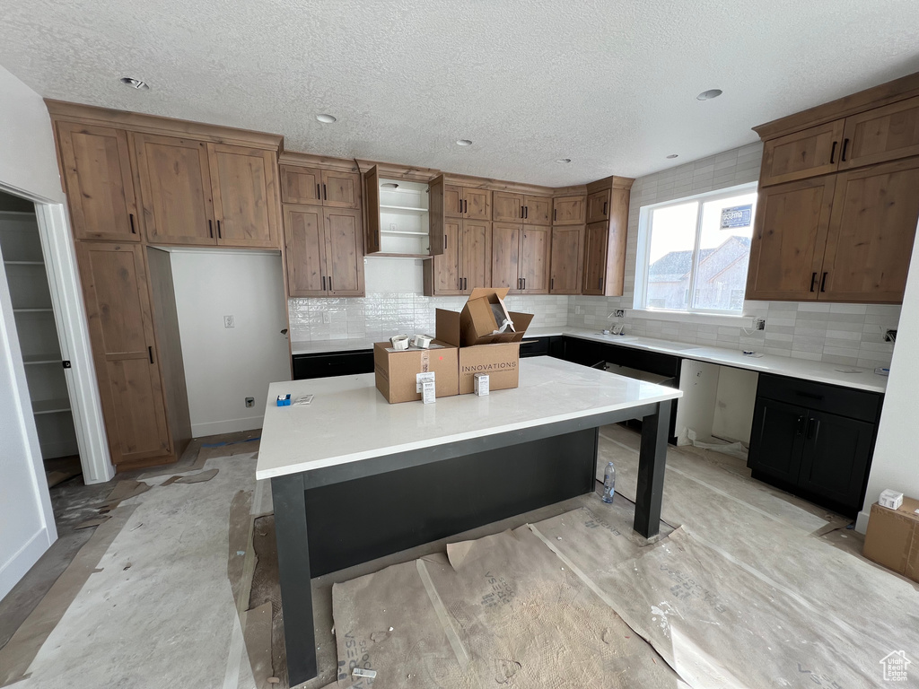 Kitchen featuring decorative backsplash, a textured ceiling, a breakfast bar area, and a kitchen island