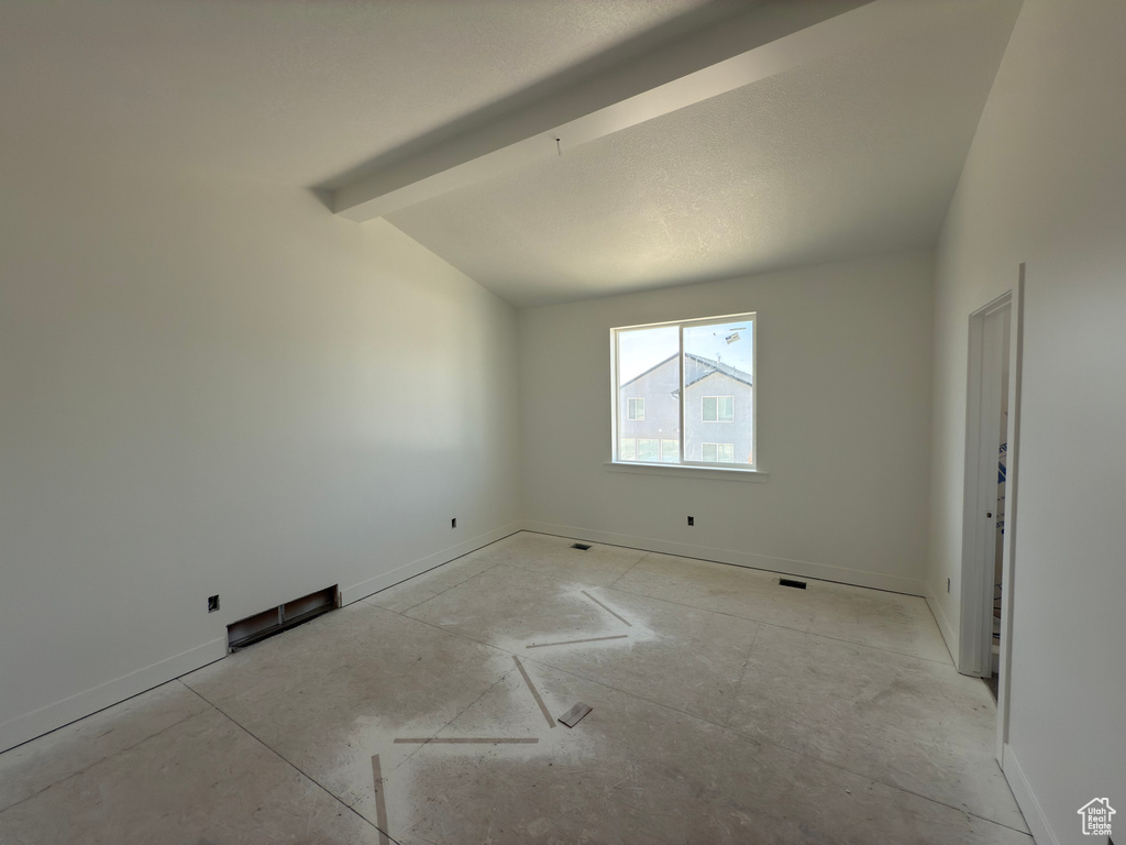 Empty room featuring lofted ceiling with beams