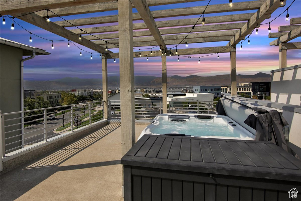 Patio terrace at dusk featuring an outdoor hot tub, a balcony, and a pergola