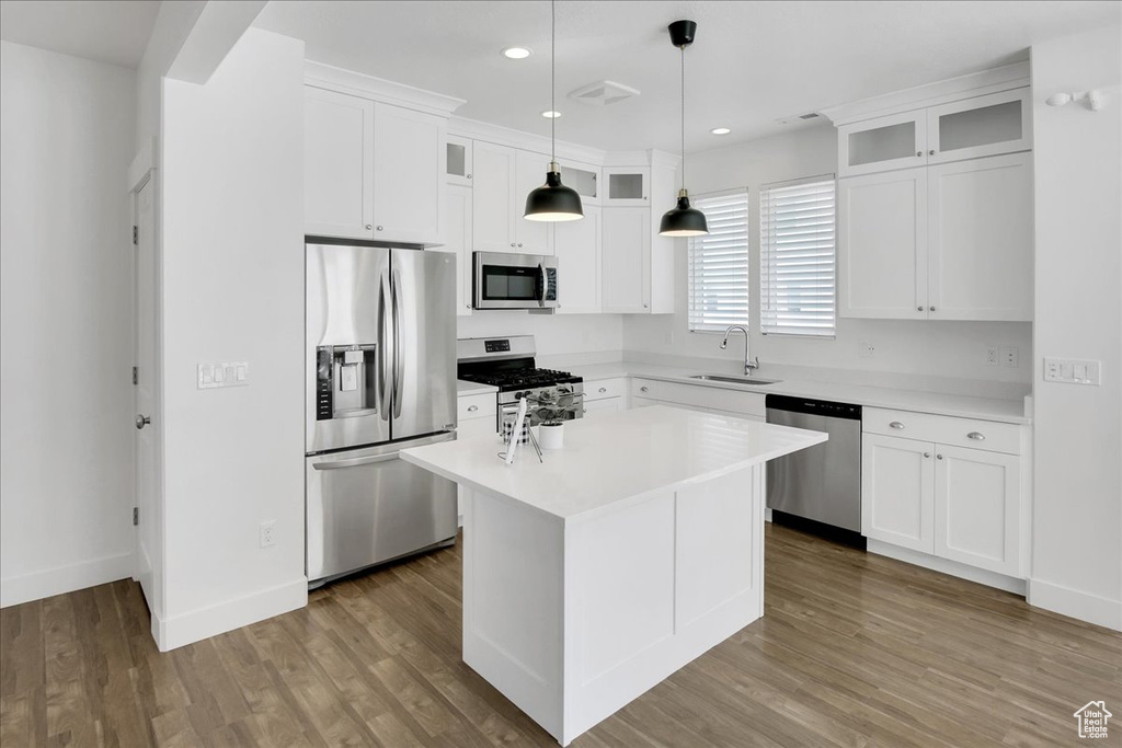 Kitchen with a kitchen island, decorative light fixtures, hardwood / wood-style floors, stainless steel appliances, and white cabinets