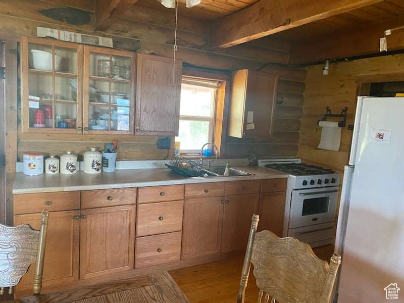 Kitchen with light wood-type flooring, white appliances, wooden walls, and beamed ceiling