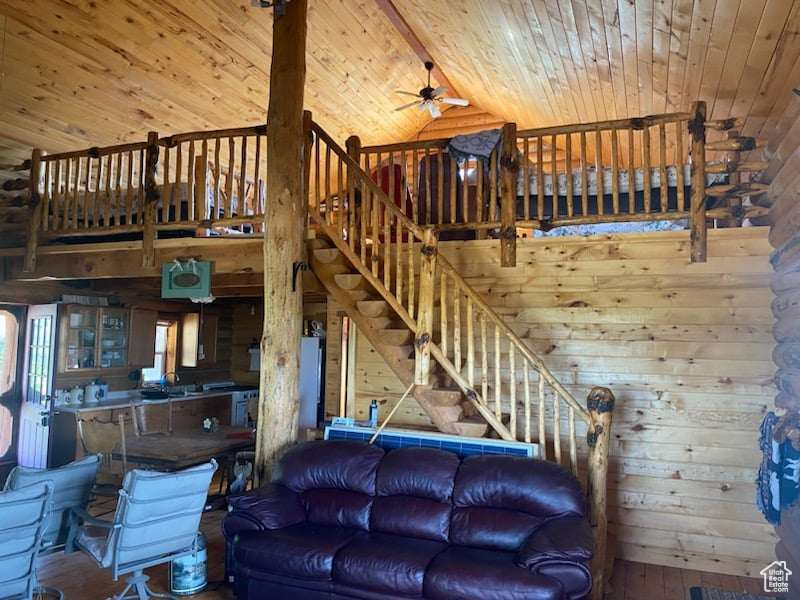 Living room featuring wooden walls, wood ceiling, wood-type flooring, ceiling fan, and beam ceiling