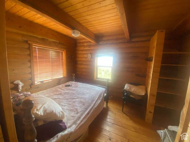 Bedroom with rustic walls, hardwood / wood-style floors, wood ceiling, and beam ceiling