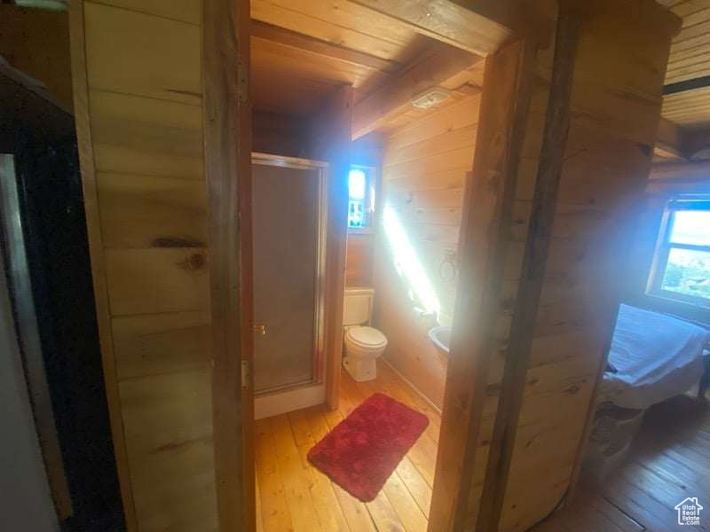 Bathroom with a shower with door, wooden walls, wood ceiling, toilet, and wood-type flooring