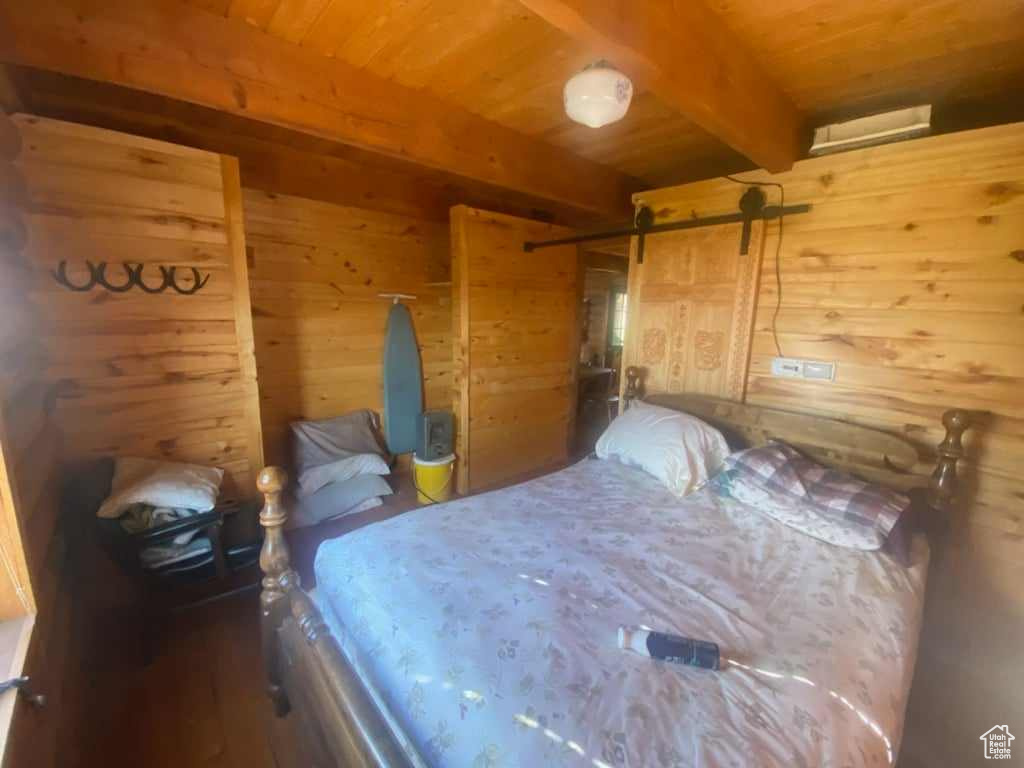 Bedroom featuring wooden ceiling, beamed ceiling, wooden walls, and a barn door