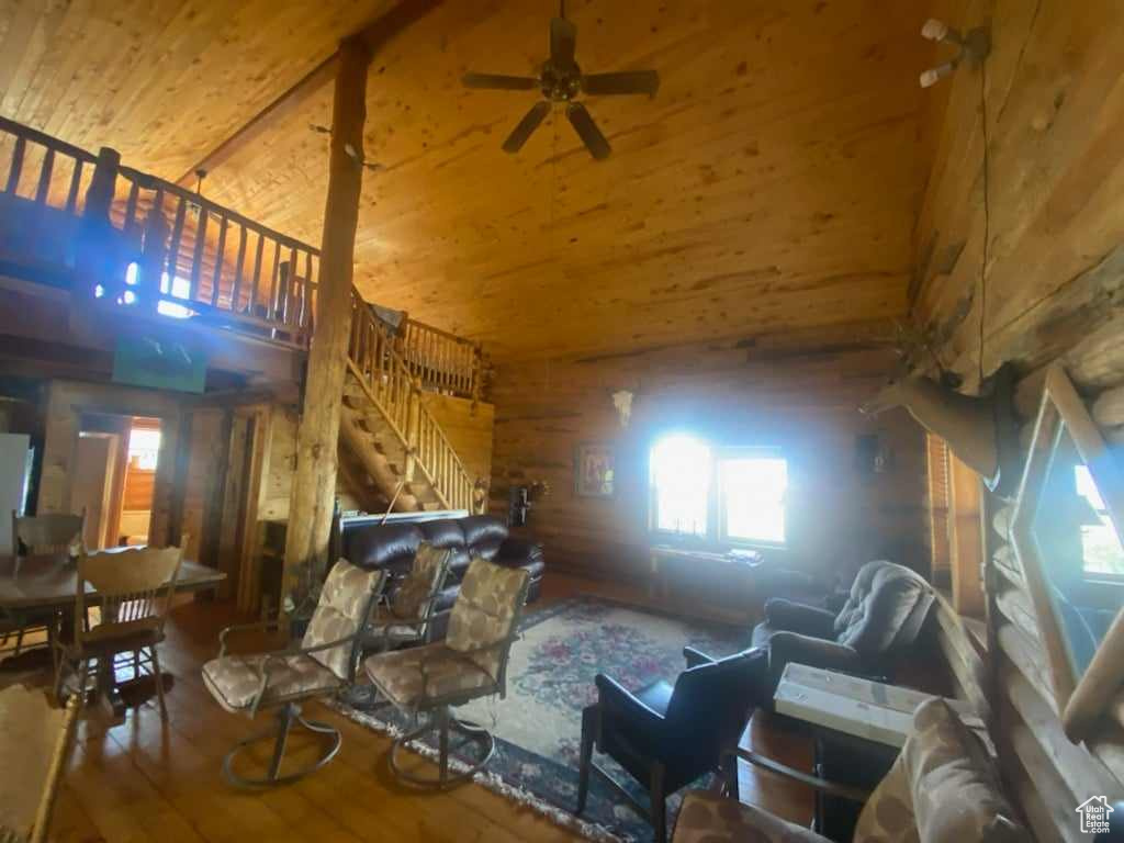 Living room featuring hardwood / wood-style flooring, wood ceiling, ceiling fan, wood walls, and high vaulted ceiling