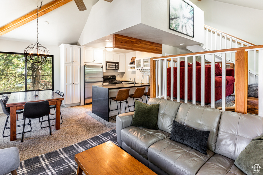 Living room with an inviting chandelier, high vaulted ceiling, beam ceiling, and light colored carpet