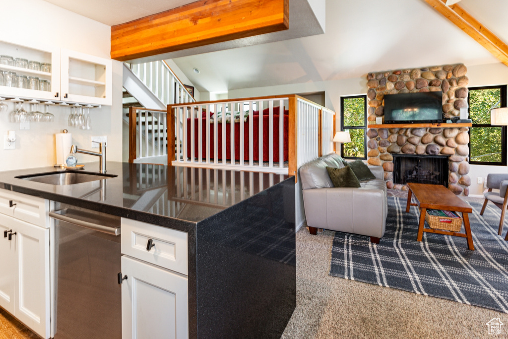 Kitchen with white cabinets, light colored carpet, beamed ceiling, sink, and a stone fireplace