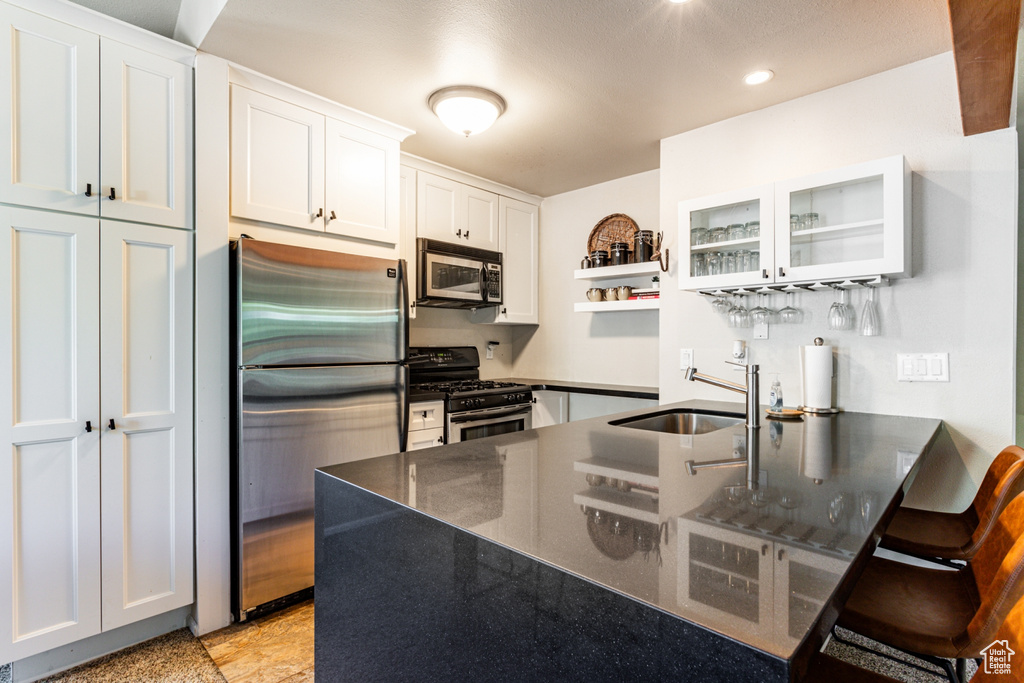 Kitchen featuring white cabinets, appliances with stainless steel finishes, a kitchen breakfast bar, and sink