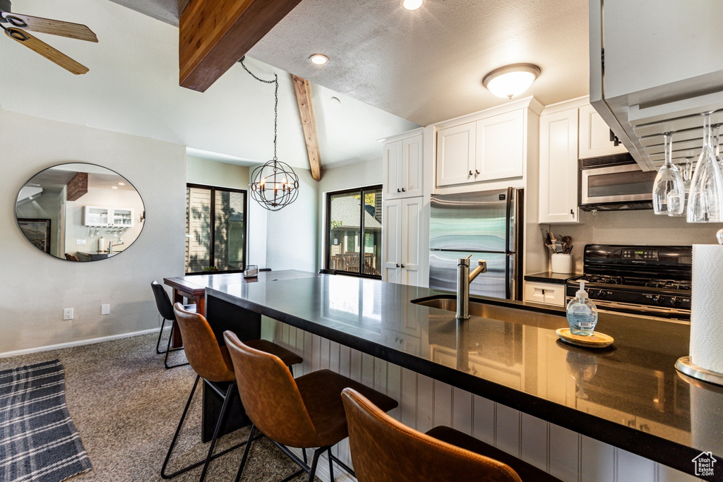 Kitchen featuring appliances with stainless steel finishes, white cabinetry, a kitchen bar, and carpet floors