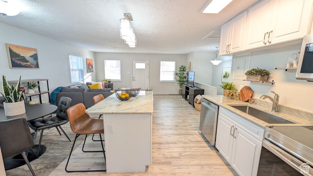 Kitchen with decorative light fixtures, a kitchen island, white cabinetry, and appliances with stainless steel finishes