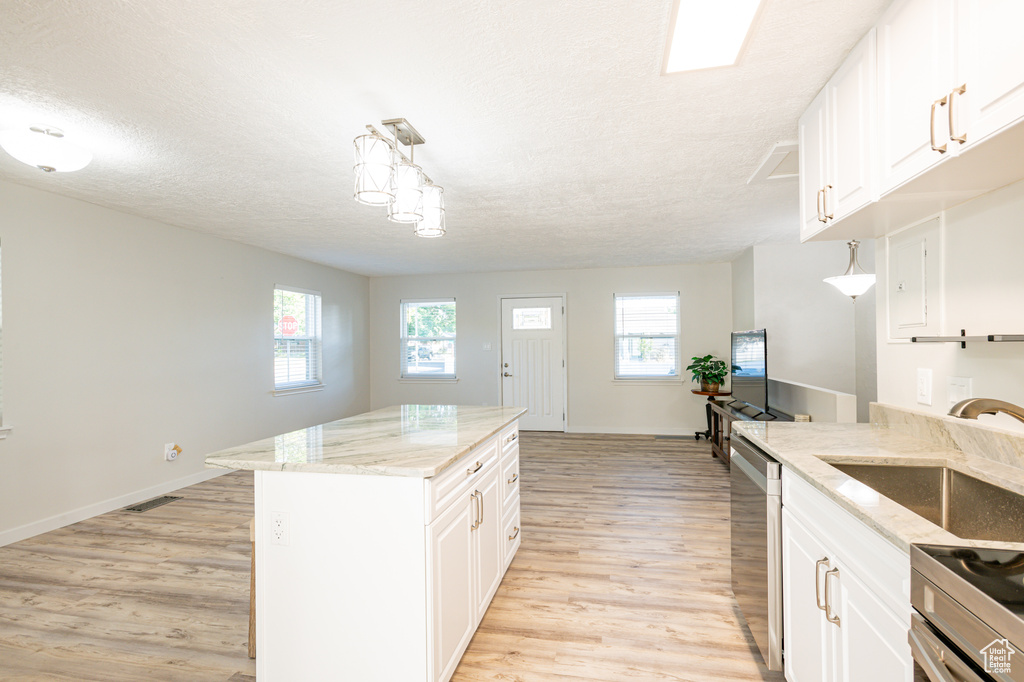 Kitchen featuring a wealth of natural light, light hardwood / wood-style flooring, light stone countertops, and decorative light fixtures