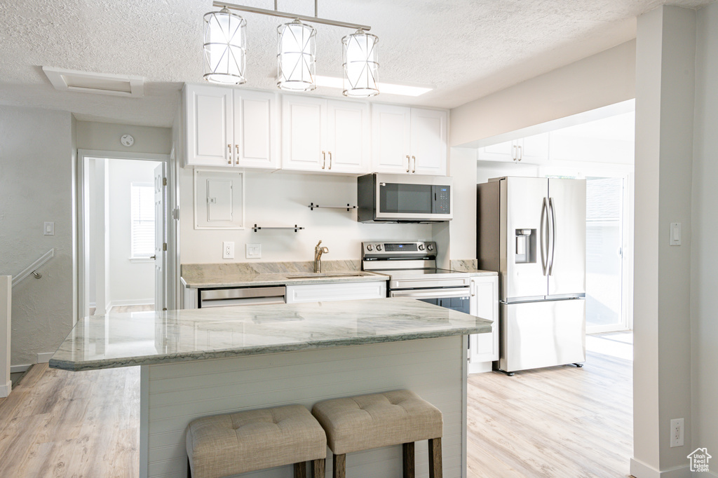 Kitchen featuring appliances with stainless steel finishes, light stone counters, light hardwood / wood-style floors, white cabinetry, and a textured ceiling