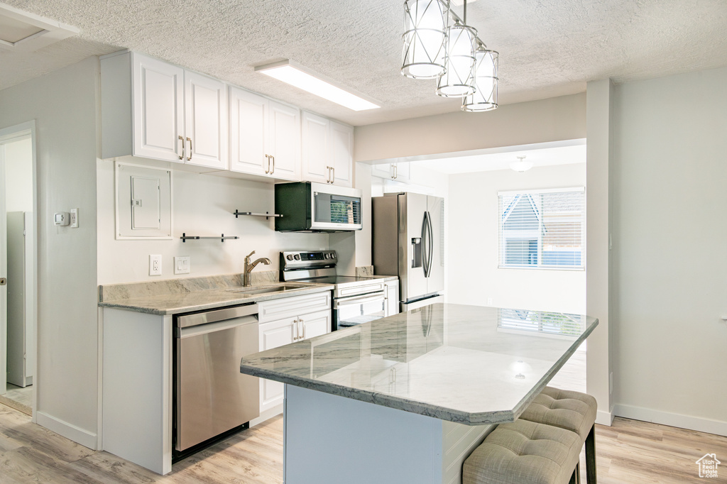 Kitchen with light stone countertops, light hardwood / wood-style flooring, appliances with stainless steel finishes, a breakfast bar, and white cabinets