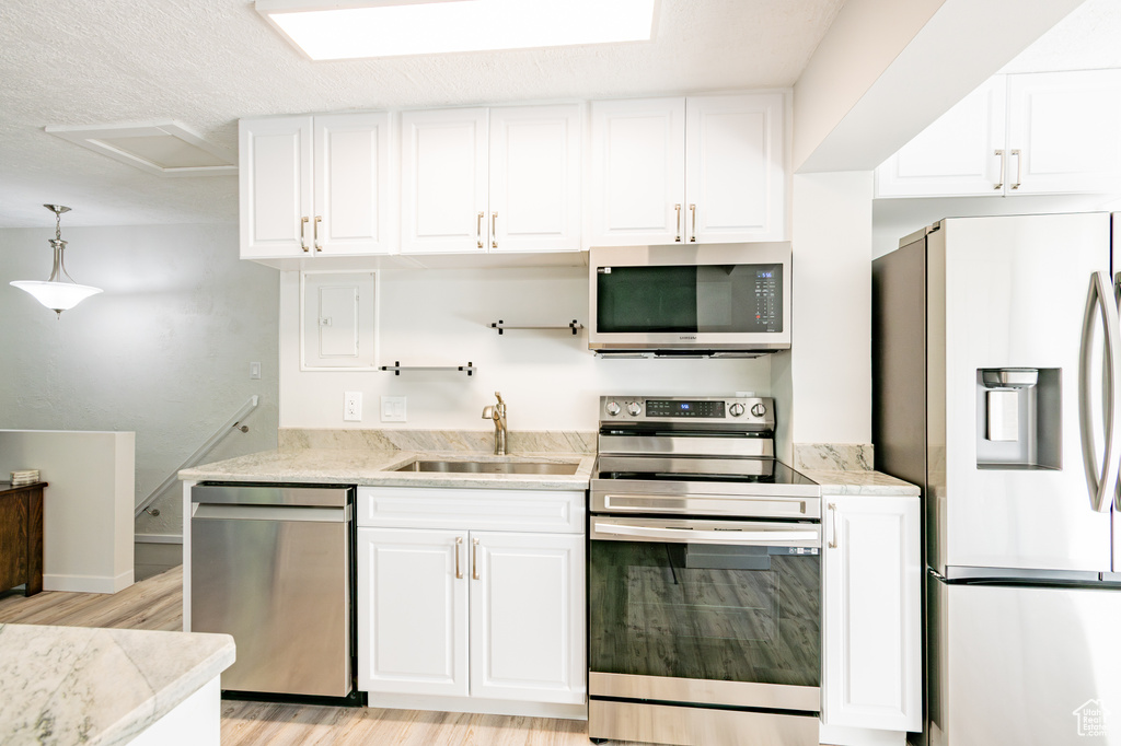 Kitchen with light wood-type flooring, white cabinetry, light stone counters, sink, and appliances with stainless steel finishes