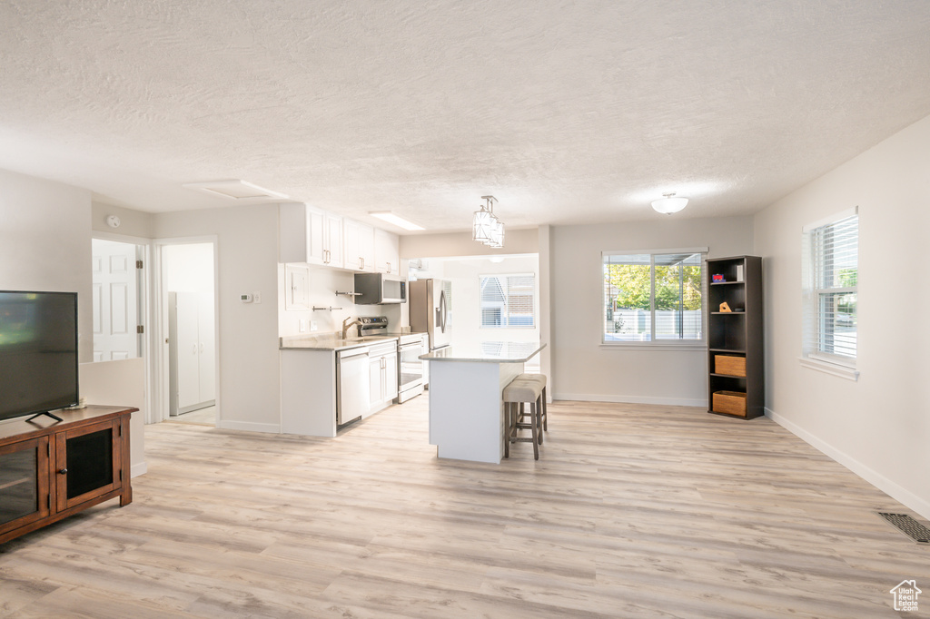 Kitchen featuring white cabinets, appliances with stainless steel finishes, a kitchen bar, and light hardwood / wood-style flooring