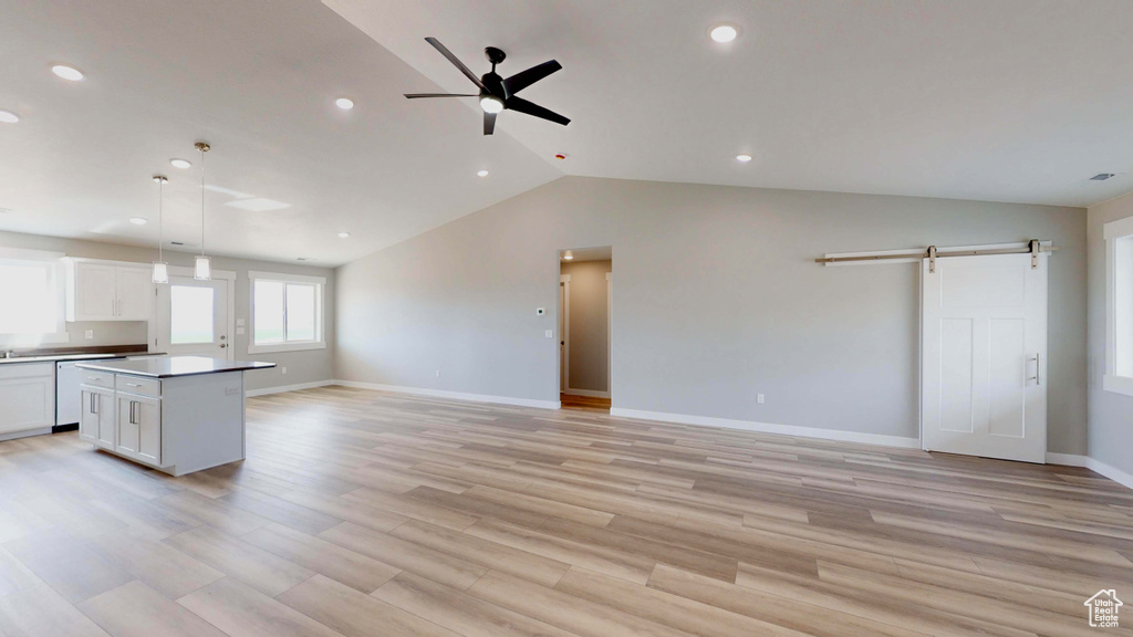 Kitchen with a barn door, light hardwood / wood-style floors, white cabinetry, ceiling fan, and a kitchen island