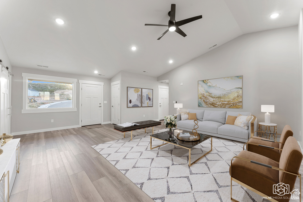 Living room with lofted ceiling, light hardwood / wood-style floors, ceiling fan, and a barn door