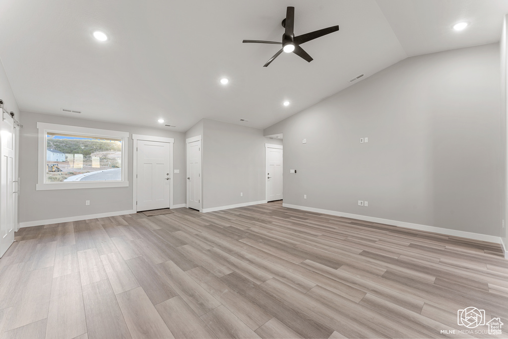 Unfurnished living room with a barn door, lofted ceiling, light hardwood / wood-style floors, and ceiling fan