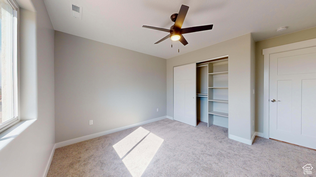 Unfurnished bedroom with multiple windows, ceiling fan, light colored carpet, and a closet